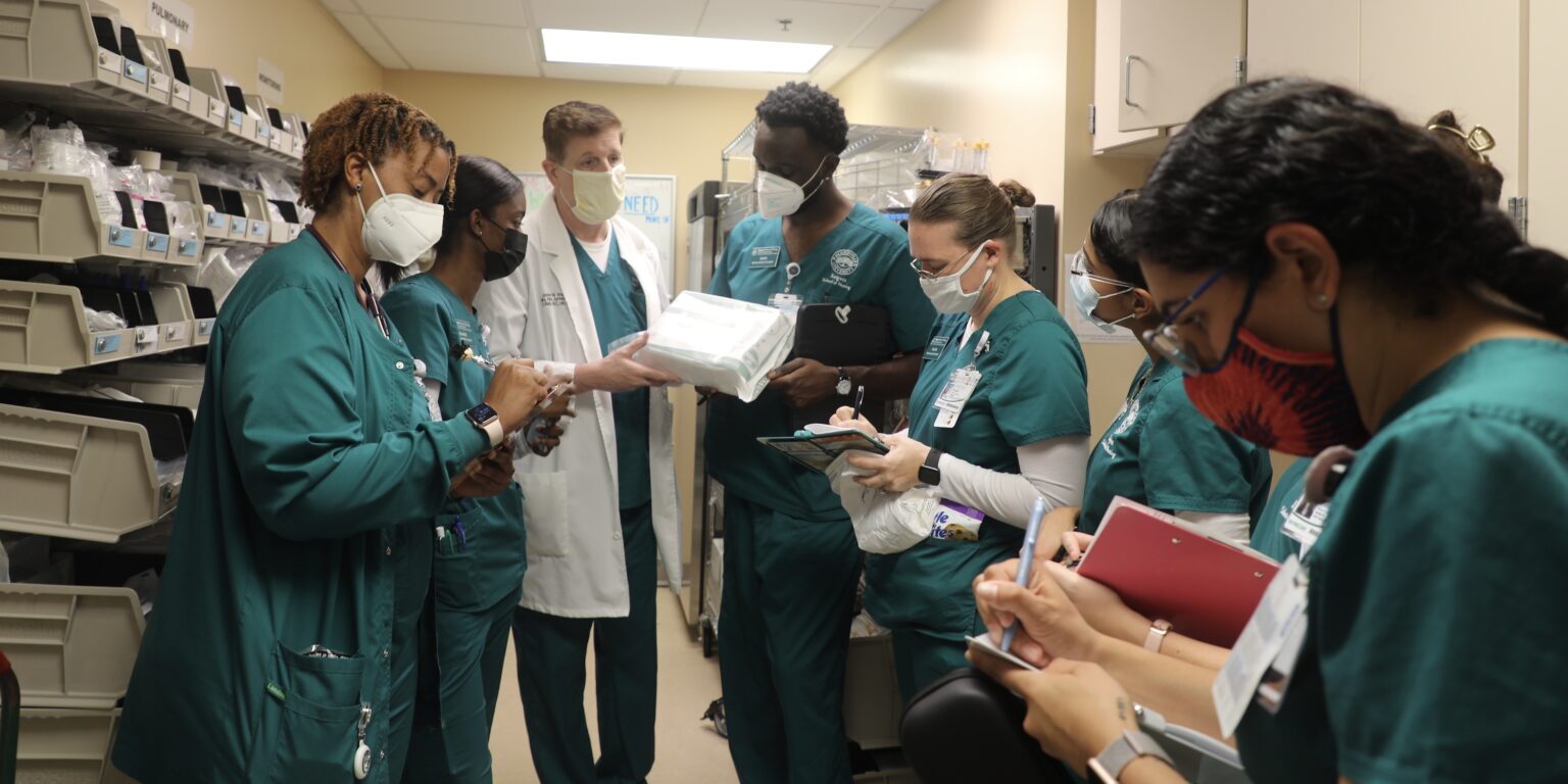 A group of nursing students standing in a supply room with an instructor.