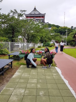 Two female students kneeling by a flower garden in front of Atami Castle