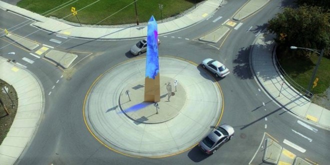 a roundabout with three cars going around, and an art sculpture in the middle in blue