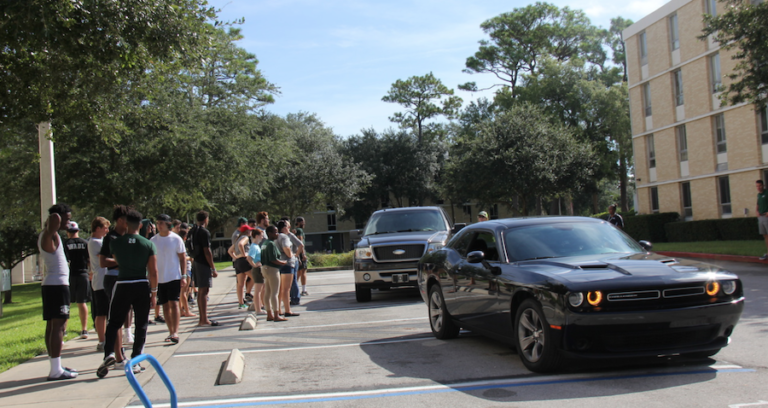 Students waiting near a car line to unpack upcoming cars on move-in day