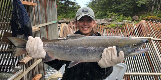 Female scientist holding sockeye salmon in front of a dam