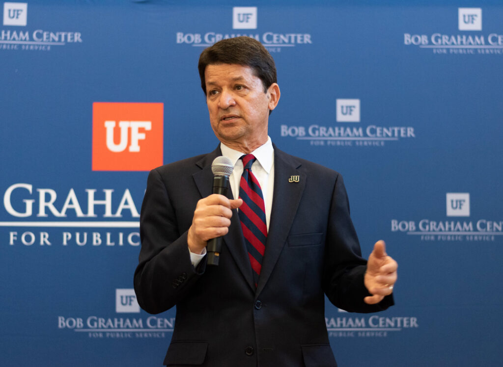 Dark headed middle aged man, Richard Mullaney, talking behind a podium in front of a banner that reads "Bob Graham Policy Center"