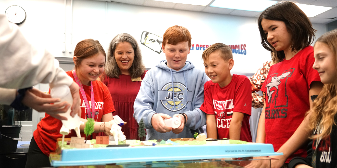 Students are smiling at an educational model surrounding one teacher