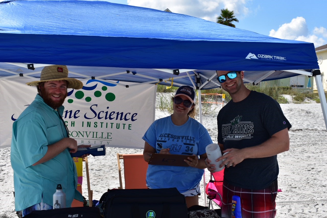 Marine research underway. Three individuals standing under a tent and smiling.