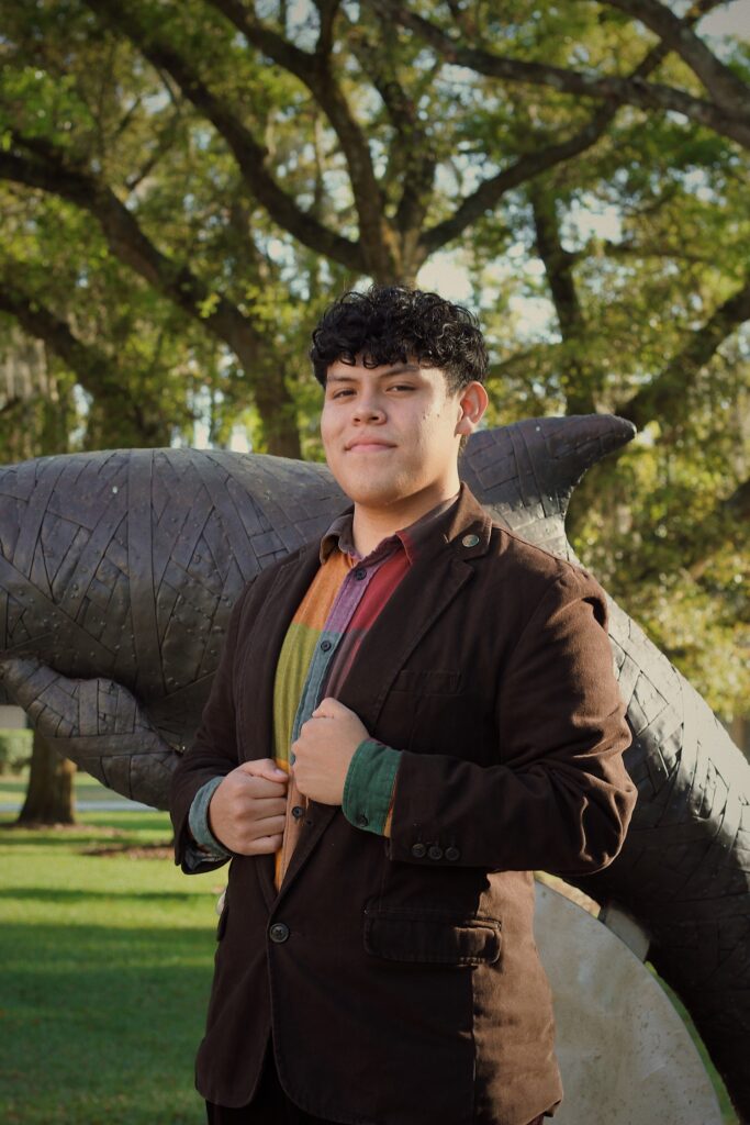 Sophomore student Bradley Cordero standing in front of a dolphin statue