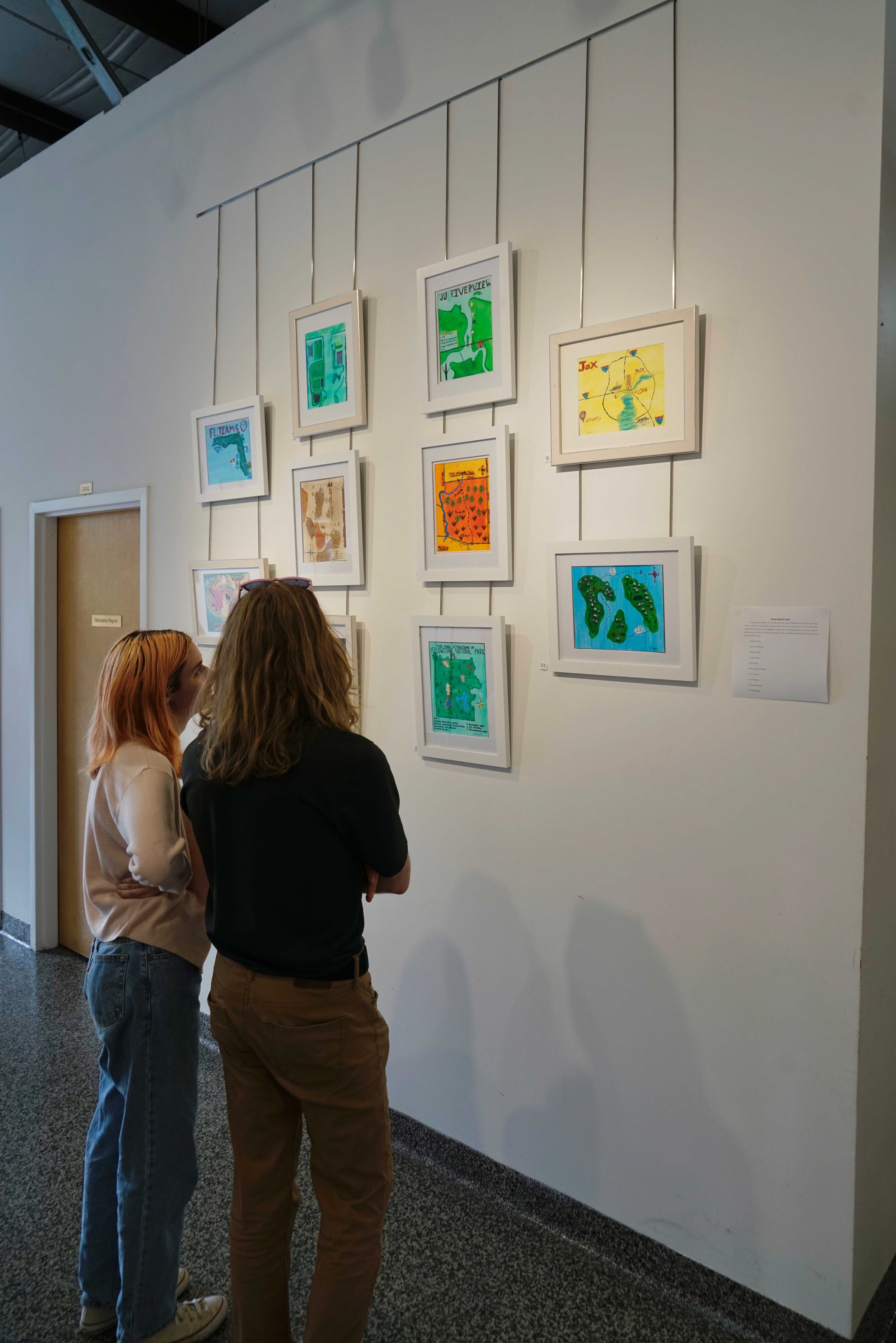 two students gaze at a gallery wall of colorful maps