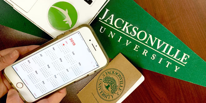 An iPhone displaying a calendar. Jacksonville University branded items in the background.