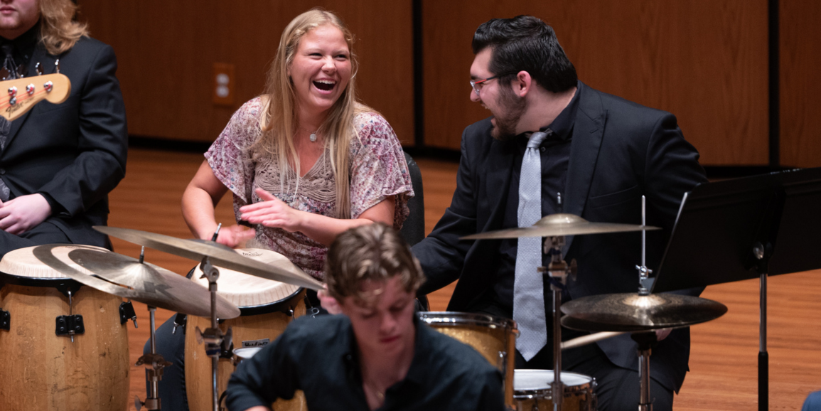 two nicely dressed students laughing at each other while playing instruments on stage