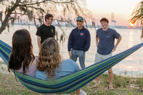 Students sitting in hammock at sunset on campus with other students