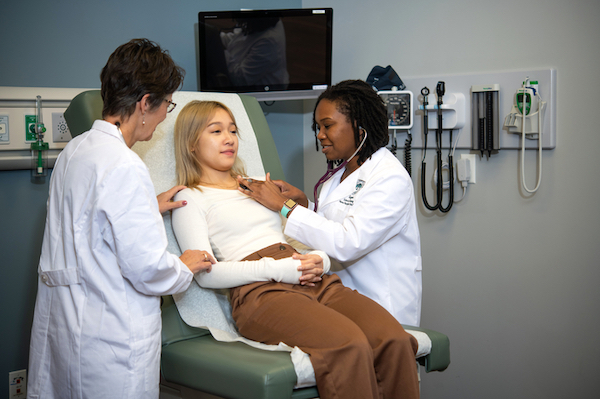 A nursing educator helping a nursing student care for a patient.