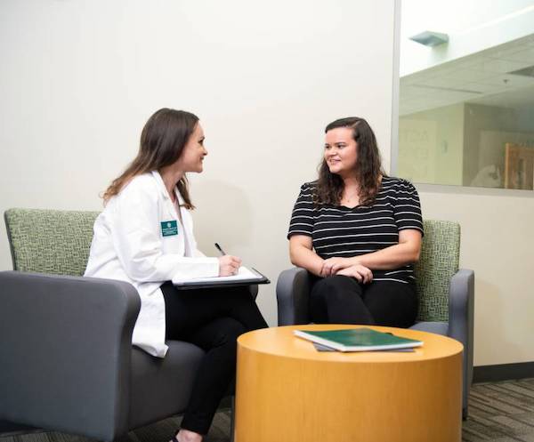 A nurse speaking with a patient while writing information on her tablet.