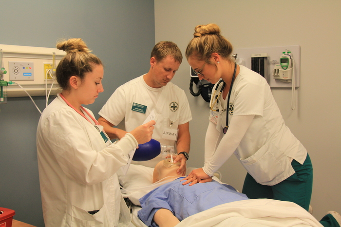 Three nursing students practicing CPR on a mannequin in a simulation center.