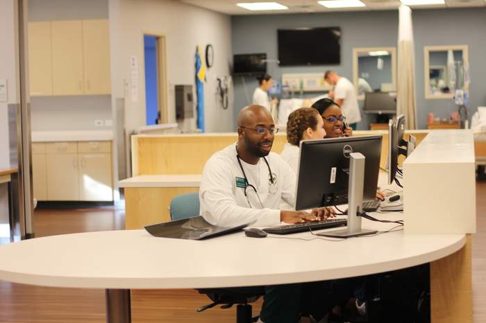 A male nurse working at a computer at a nurse's station.