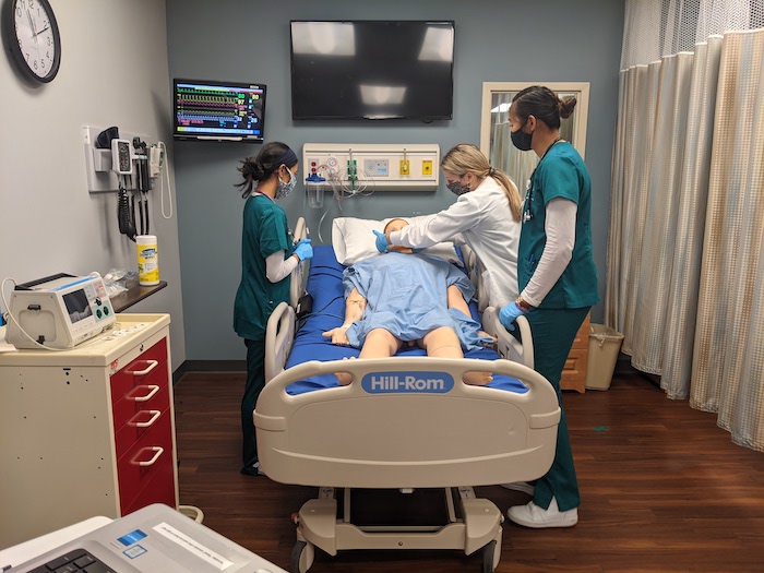 Three nursing student practicing on a model patient in a simulation center.