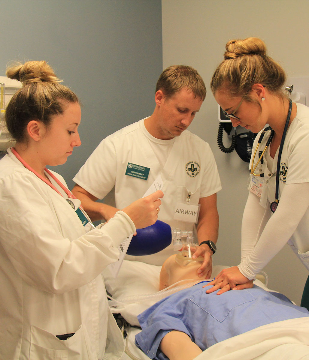 Three students practice on a mannequin in the Simulation Center.
