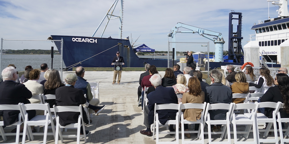 People at talk with ship in background