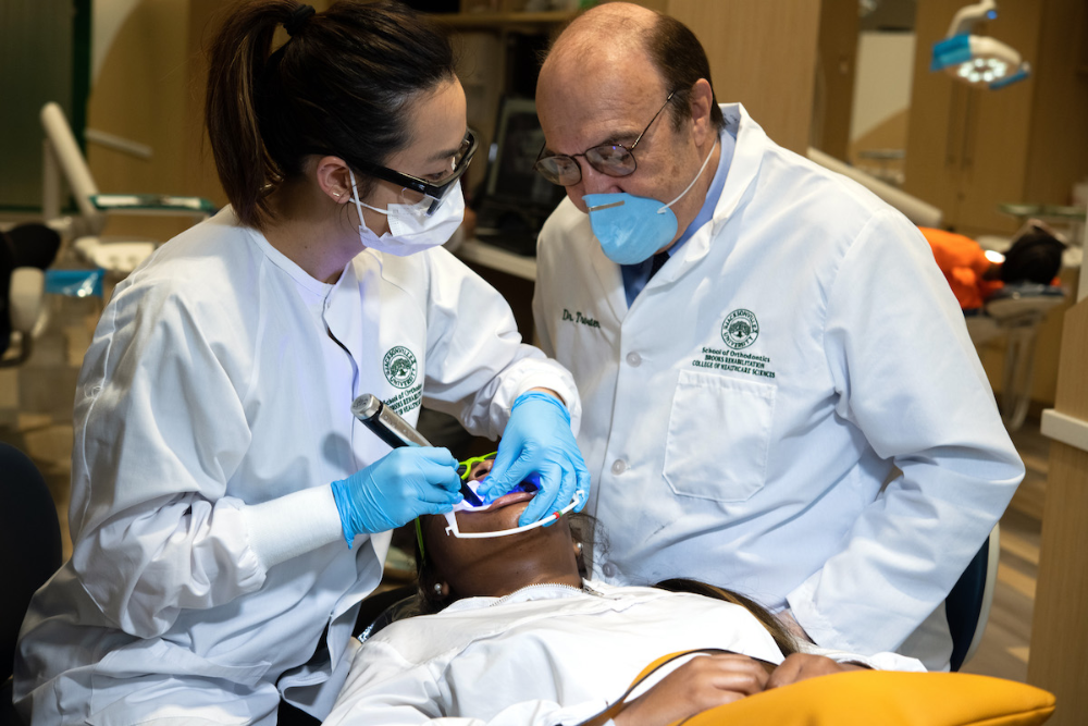 A student giving a patient a dental exam, as a professor watches.