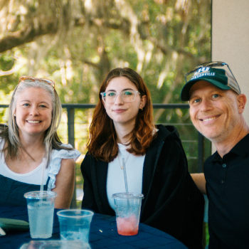 A student and their parents seated at a table facing the camera smiling.