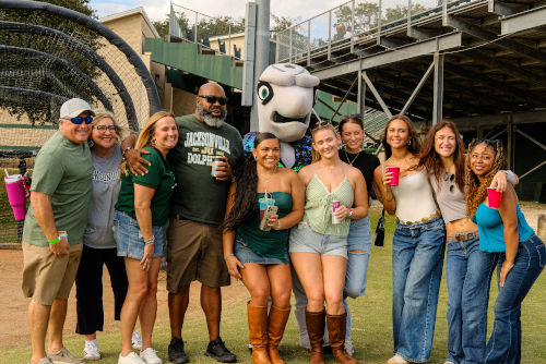 A group of students with Dunk'n JU's Mascot posing at the football field