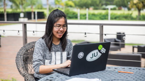 A student sitting outdoors with their laptop on a table