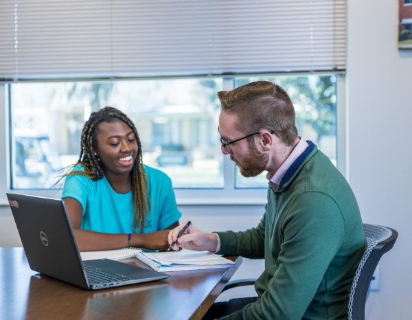 A student and counselor seated at a work desk with papers and a laptop