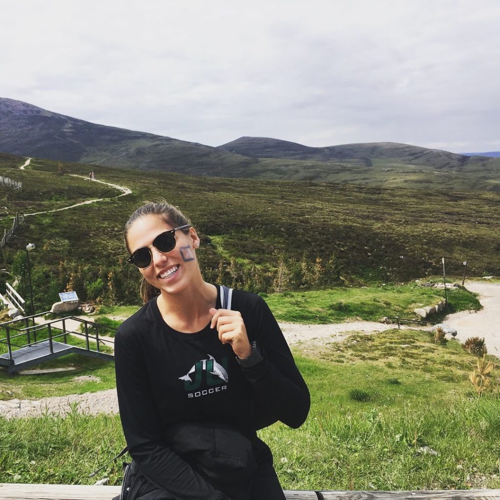 Natalia smiling for the camera in front of the Scottish countryside.