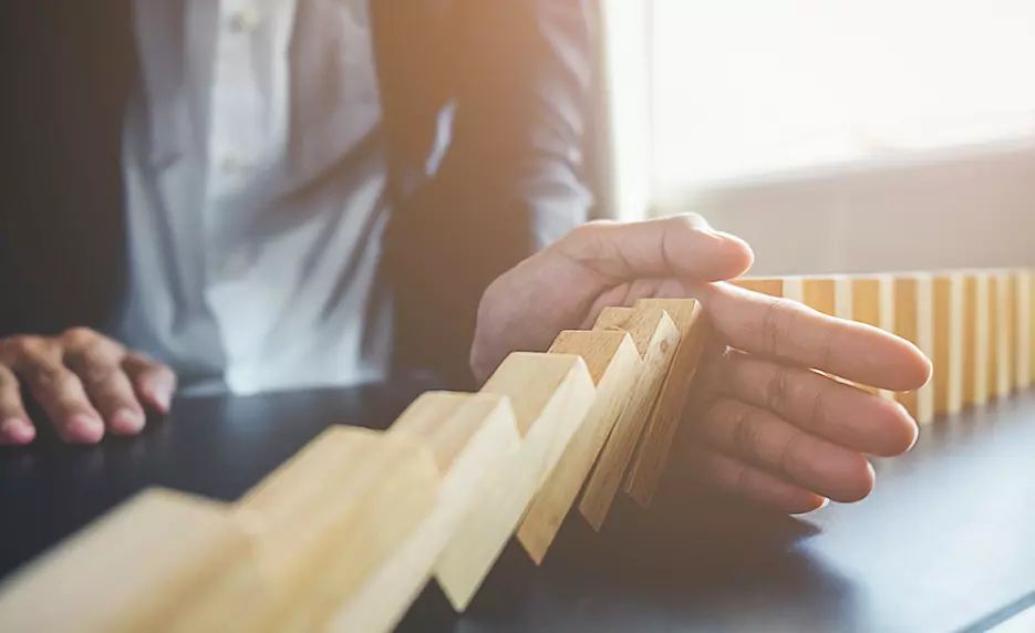 Businessman's hand blocking wooden blocks from falling over