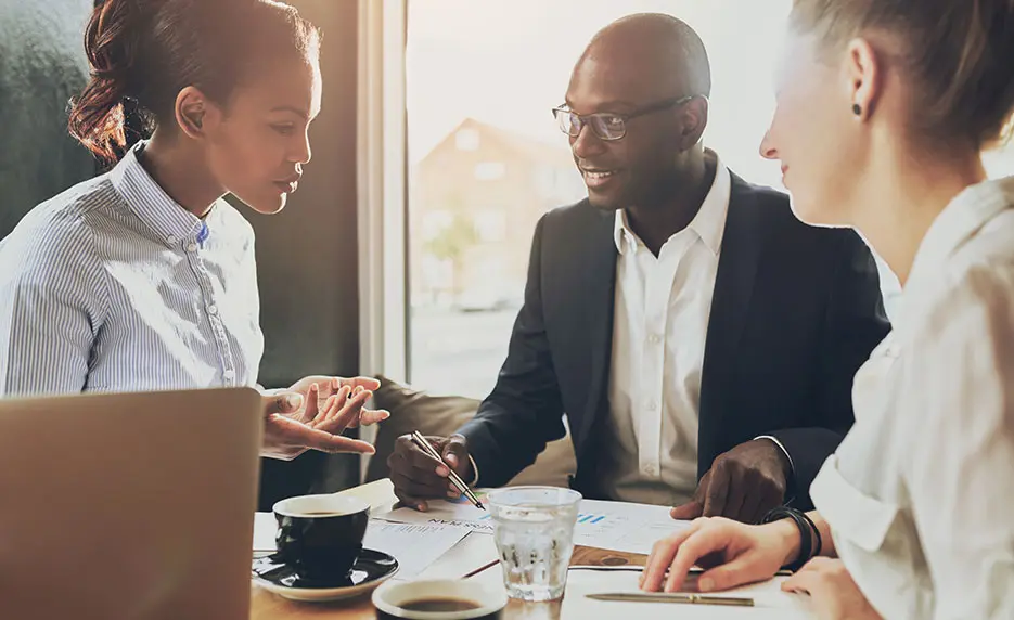 Three business people discuss the data listed on papers in front of them