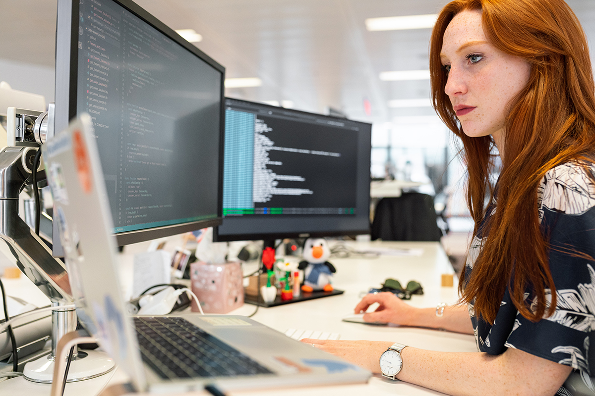 Information technology professional sitting at a desk with several monitors working on code