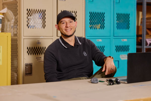 Zak Rabani featured seating at a computer desk in front of a cabinet with artwork materials